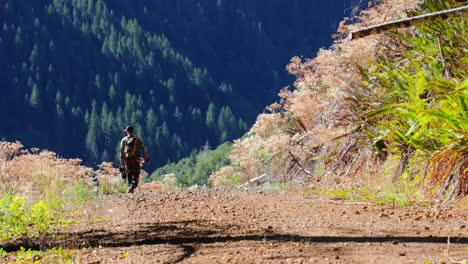 man walks toward mountain wilderness in hunting gear with a bow