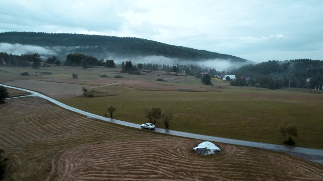 텅 빈 안개가 자욱한 도로에서 움직이는 은색 자동차의 공중 샷