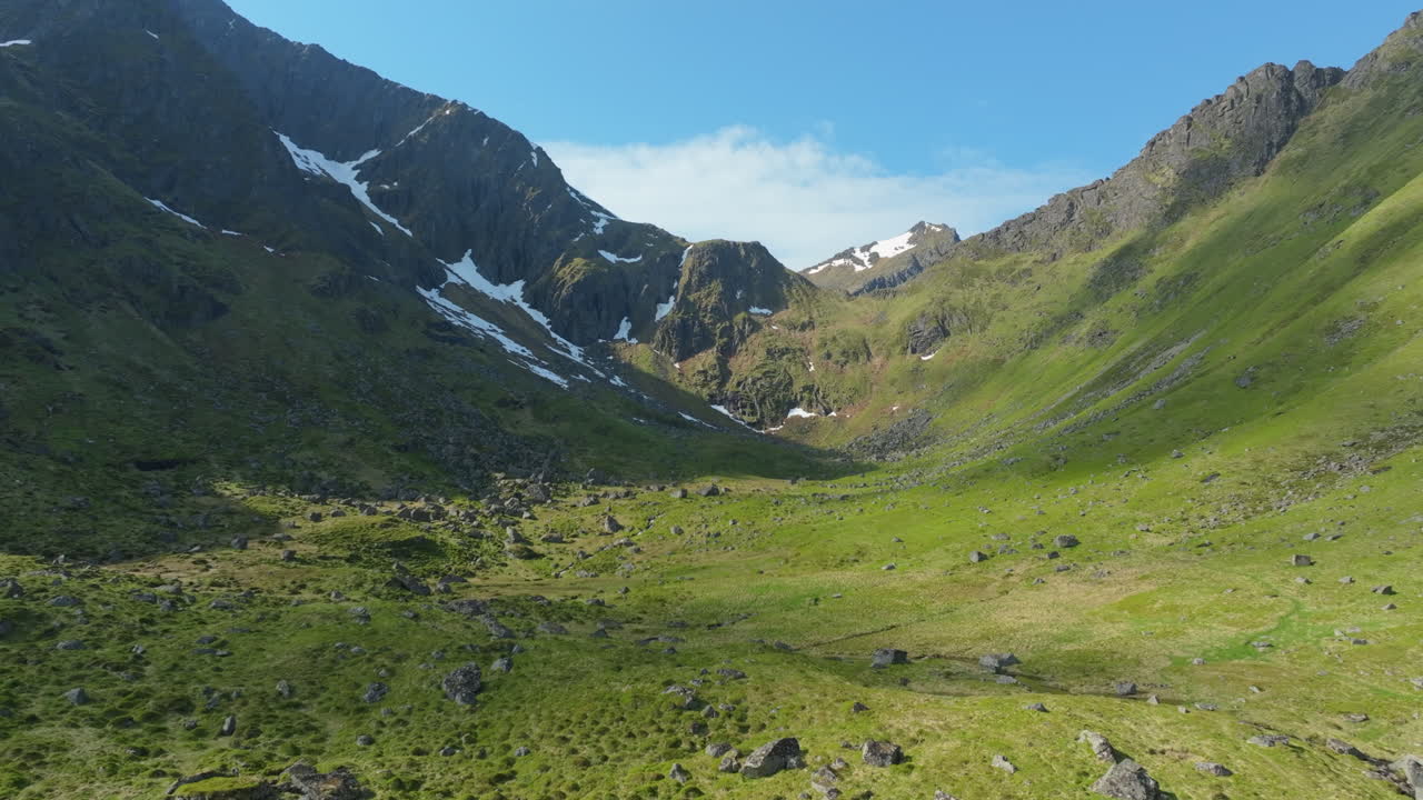 Grønn dal omgitt av fjell med snøflekker under en klar blå himmel på Lofoten, Norge
