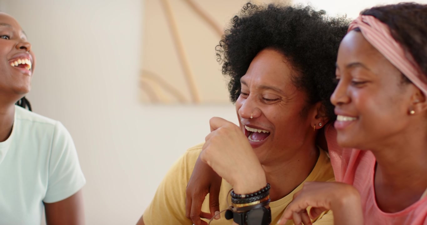 Three African women laughing and leaning after pointing at pizza, reaching for slices and water