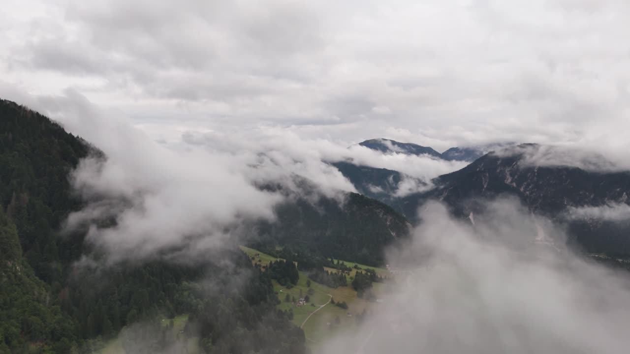 Drone flies through clouds over green Alps mountains on a cloudy day showcasing natural beauty