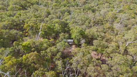 Vista-Aérea-De-Una-Pequeña-Cabaña-Ubicada-Dentro-De-Un-Parque-Nacional-Rodeada-De-Bosque