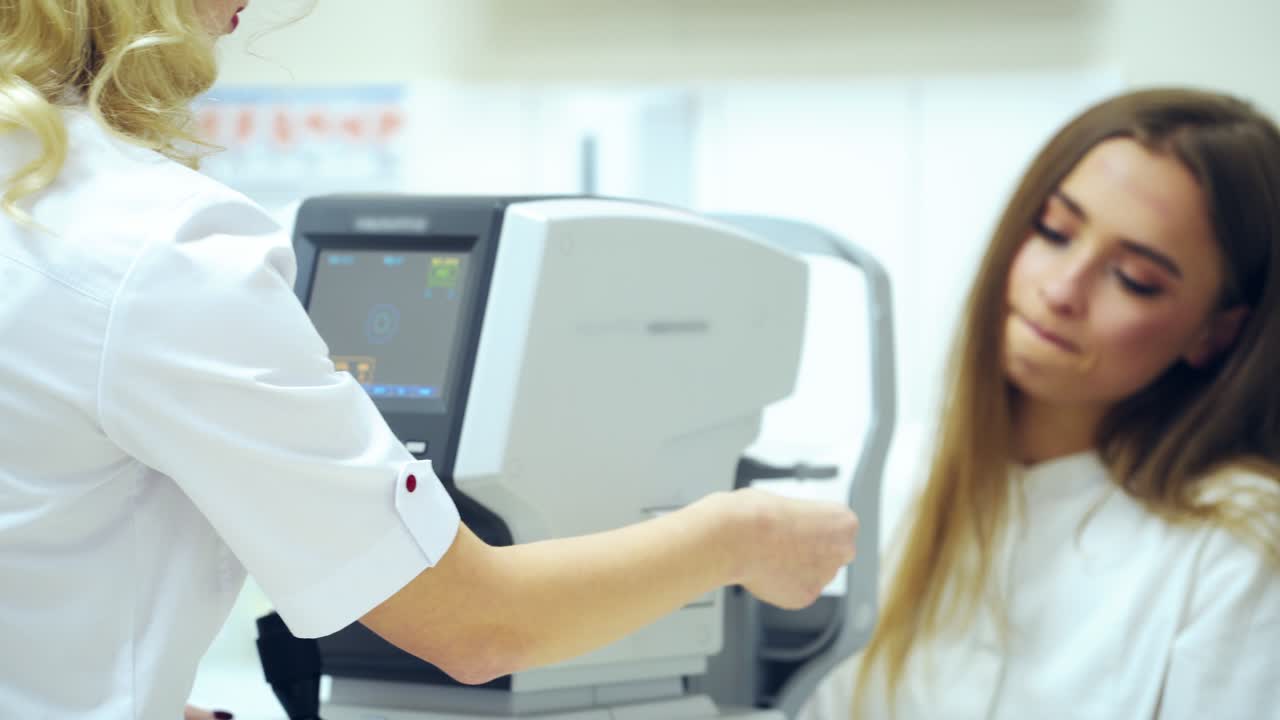 Beautiful woman checking her eyes in clinic. Refractometer tests human eyes and printing the results. Ophthalmologist examines female's eyes on modern device.