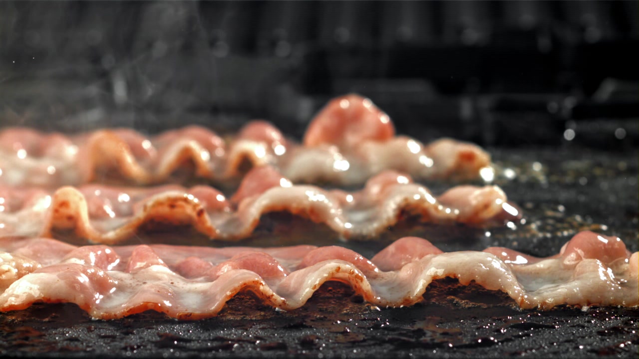 Primo piano di pancetta che sfrigola e cuoce su una piastra calda