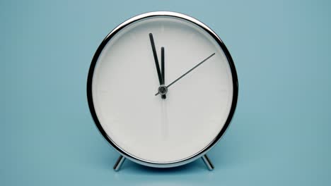 silver alarm clock isolated on a blue background, showtime 11.58 am or pm.
