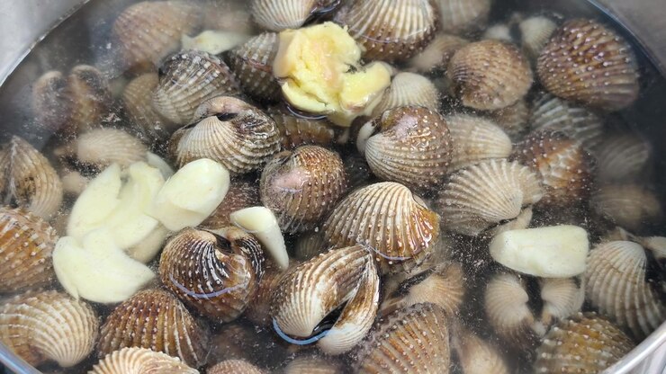 Fresh clams are boiled with garlic and aromatic herbs in a pot. This cooking process enhances rich flavors while removing unwanted fishy odors.