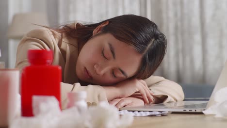 close up of sick asian businesswoman sleeping on table while working with laptop in the living room at home