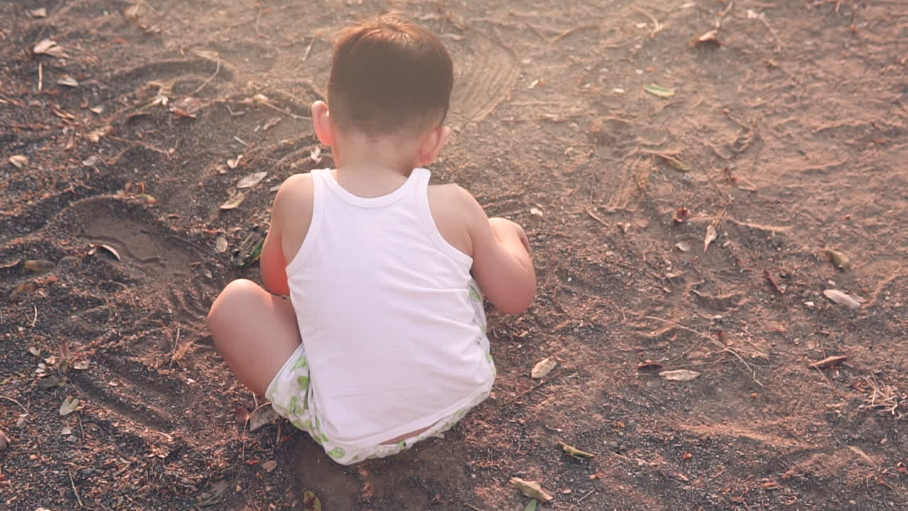 toma en ángulo alto de un joven de piel blanca y cabello negro jugando con la suciedad en la caja de arena de un parque al aire libre al atardecer en el verano