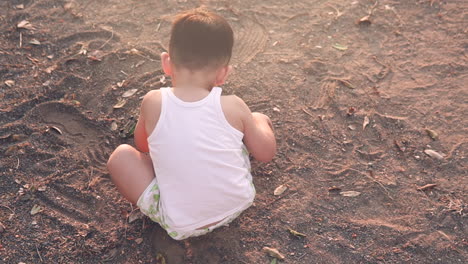 Hochwinkelaufnahme-Eines-Kleinen-Jungen-Mit-Weißer-Haut-Und-Schwarzen-Haaren,-Der-Im-Sommer-Bei-Sonnenuntergang-Im-Sandkasten-Eines-Parks-Im-Freien-Mit-Dem-Dreck-Spielt