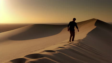 man walking on a sand dune at sunset