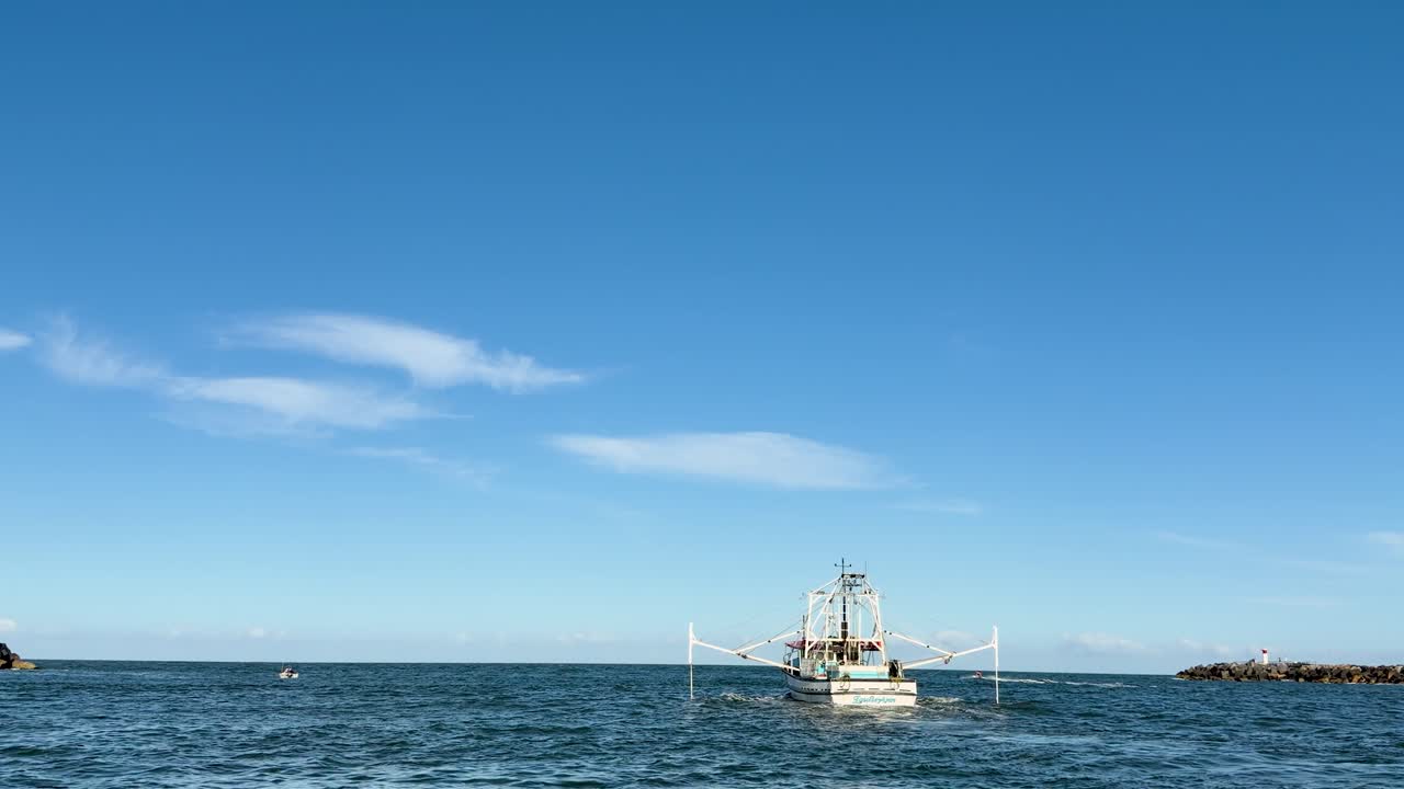 Fishing trawler moves steadily through calm river channel under clear sky, wide static shot