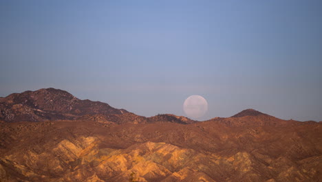 the full moon sets behind the rugged terrain in the mojave desert - time lapse