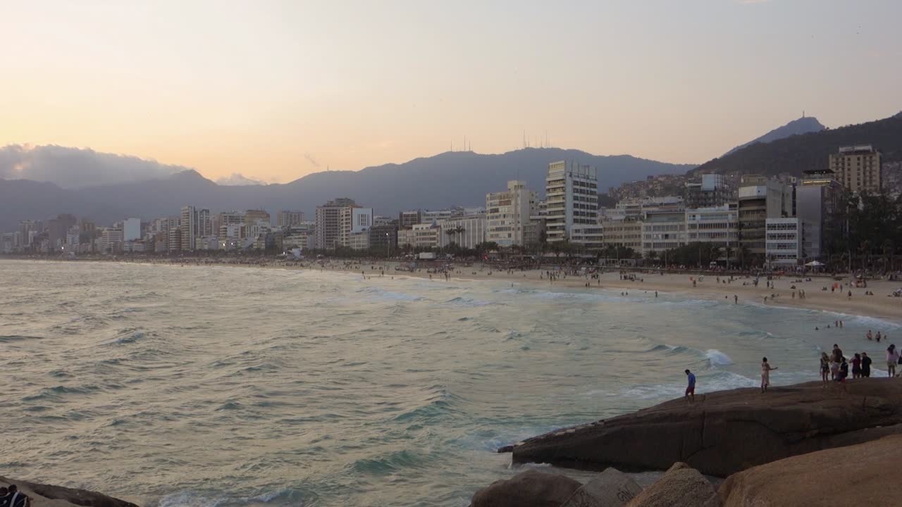 Crowd Of Tourists At The Popular Ipanema Beach In Rio de Janeiro, Brazil With Wavy Ocean At Sunset. wide