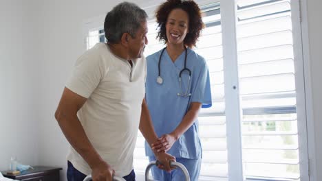 Mixed-race-female-doctor-home-visiting-helping-senior-patient-get-up