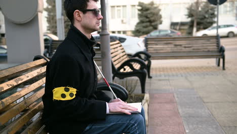Blinder-Mann-Mit-Armbinde,-Der-Ein-Braille-Buch-Liest,-Während-Er-Im-Freien-Auf-Einer-Bank-Sitzt