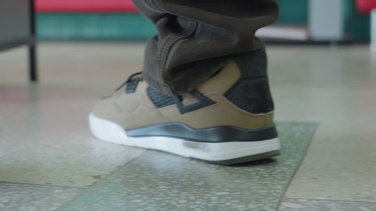 Close up of person wearing brown pants and beige sneakers walking on marble floor in library, books neatly arranged on low shelf in background