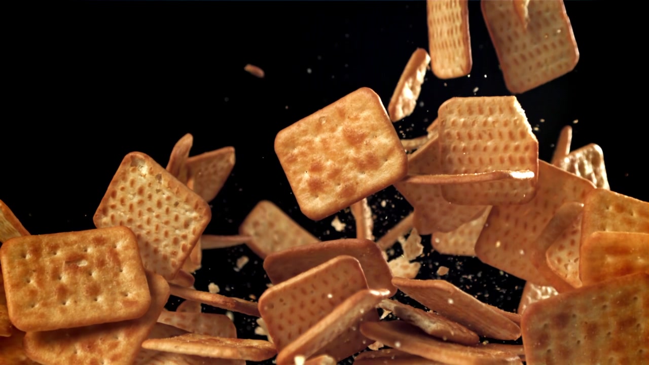 Movimento rallentato di cracker quadrati in caduta con briciole su sfondo nero