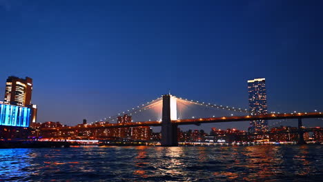 River cruise by the East River at night. View on the Pier 17 Bar and the Brooklyn Bridge from low angle perspective