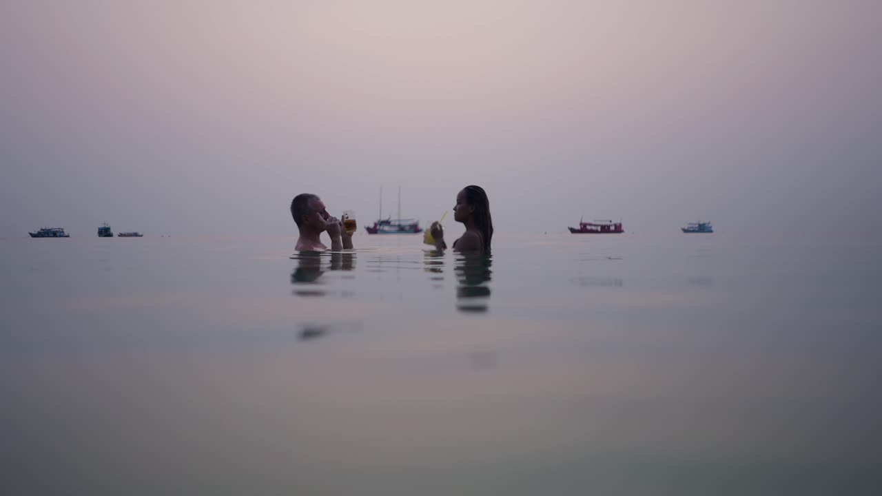 Couple enjoying drinks in the water at sunset