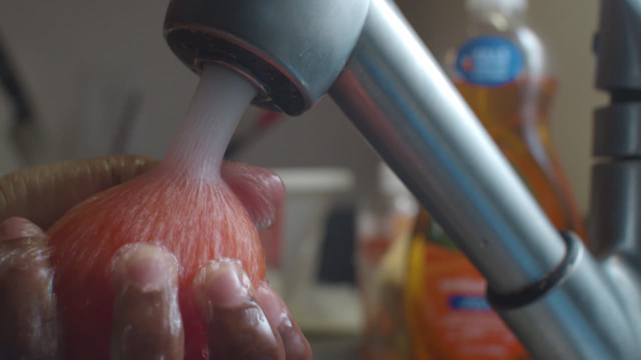 Rinsing red tomato in kitchen sink with high-pressure water - close up