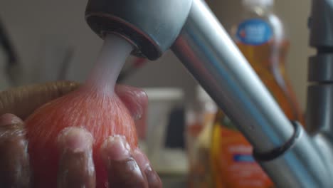 Rinsing-red-tomato-in-kitchen-sink-with-high-pressure-water---close-up