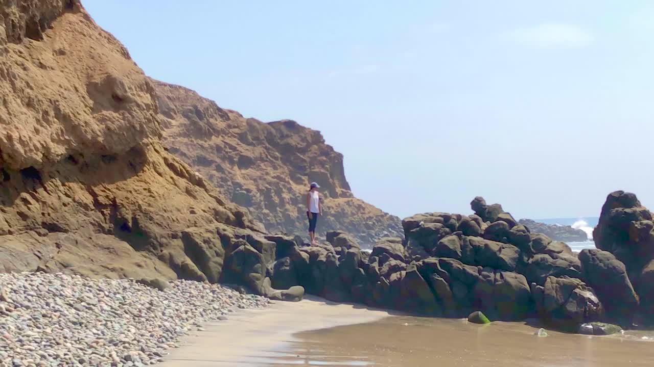 A young woman explores an empty beach surrounded by cliffs on a sunny day