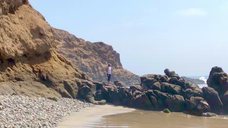 a young woman explores an empty beach surrounded by cliffs on a sunny day