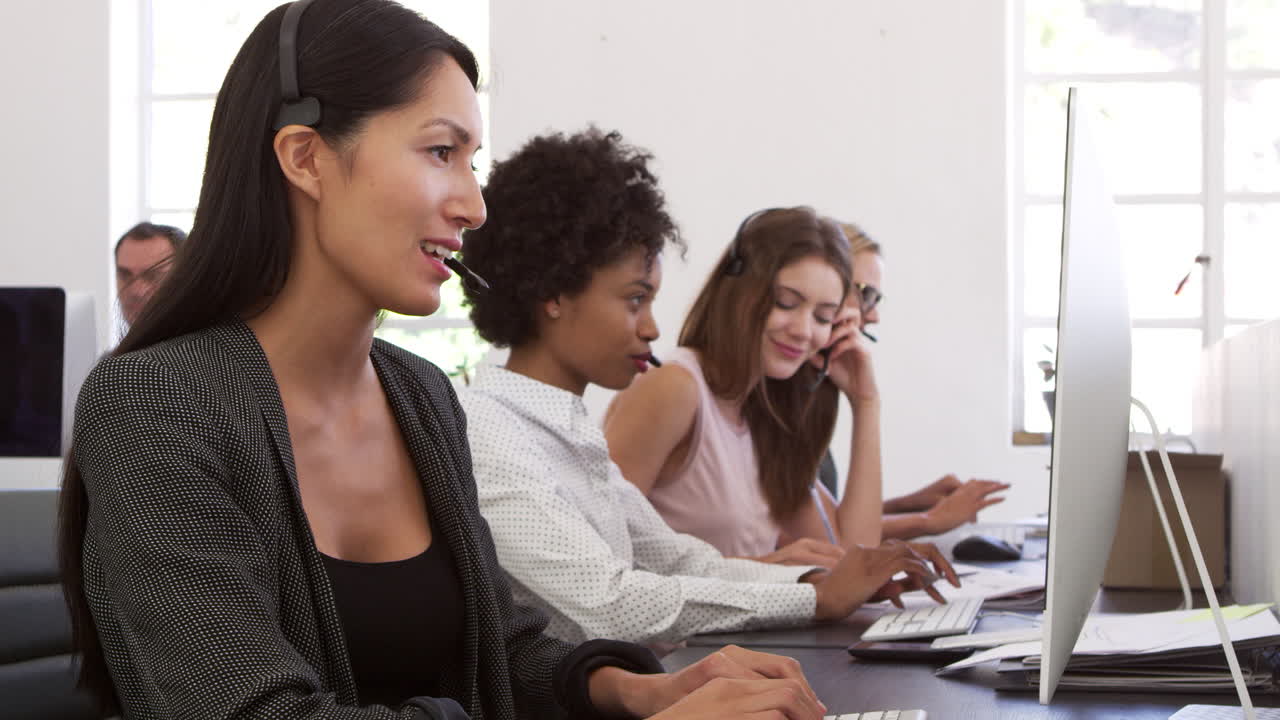 una fila de mujeres usando auriculares de teléfono en una oficina de plan abierto