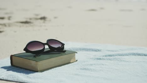 primer plano del libro, gafas de sol y toalla en la playa, en cámara lenta, con espacio para copiar