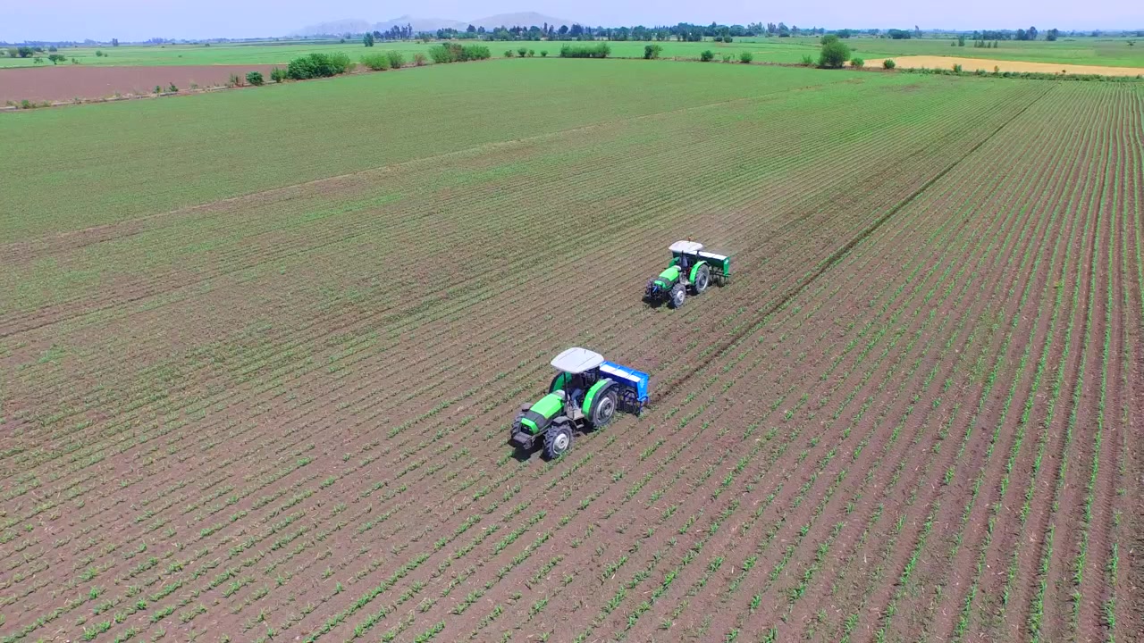 Due trattori al lavoro in un vasto campo agricolo.