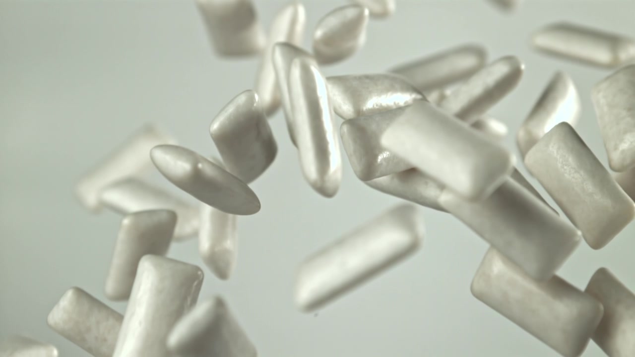 Vita tuggummibitar faller i slowmotion mot ljus bakgrund.