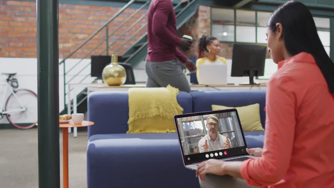 mujer biracial usando computadora portátil para videollamada, con un colega de negocios en la pantalla