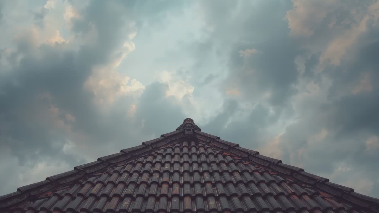 Breeze initiating drift of gray and orange clouds above house's tiled roof ridge, revealing glow