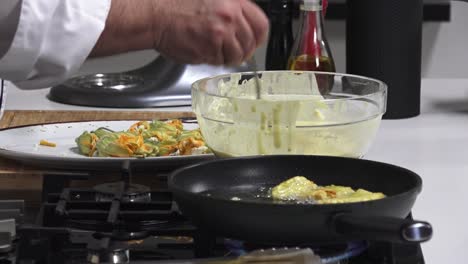 a chef prepares stuffed zucchini flowers by dipping them in batter and frying them in a pan. the kitchen is well-equipped, showcasing fresh ingredients and utensils
