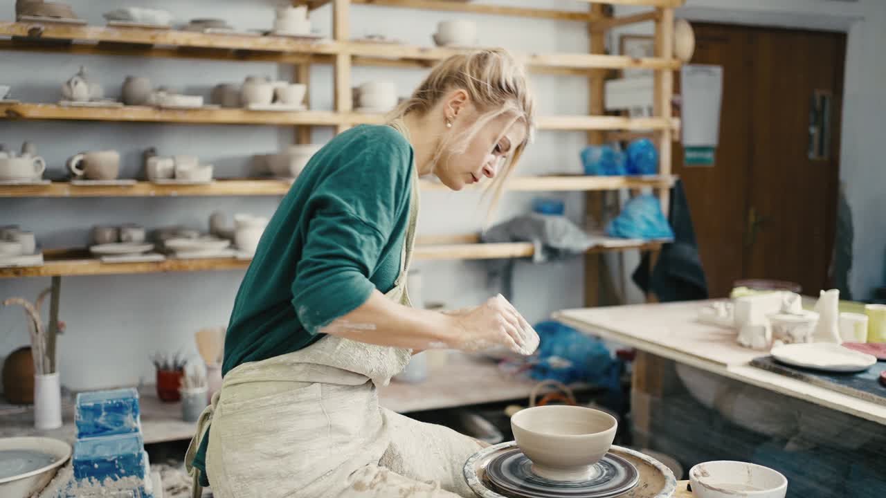 Professional woman potter making ceramic bowl on spinning wheel, working with spatula, slow motion