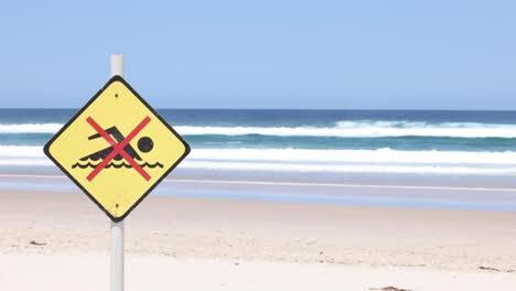 warning sign on beach against a backdrop of waves