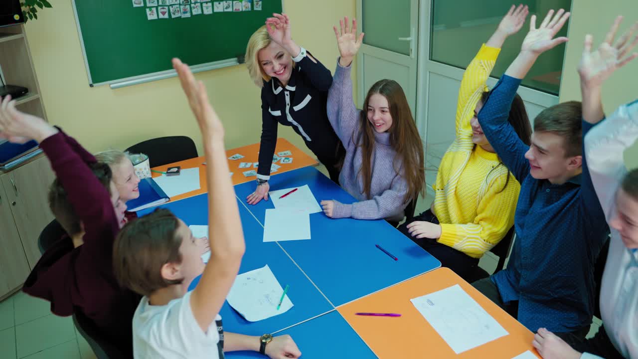 Happy children and teacher. Positive classmates and their teacher unite by hands in the classroom. Friendly students having fun together at school. Back to school.