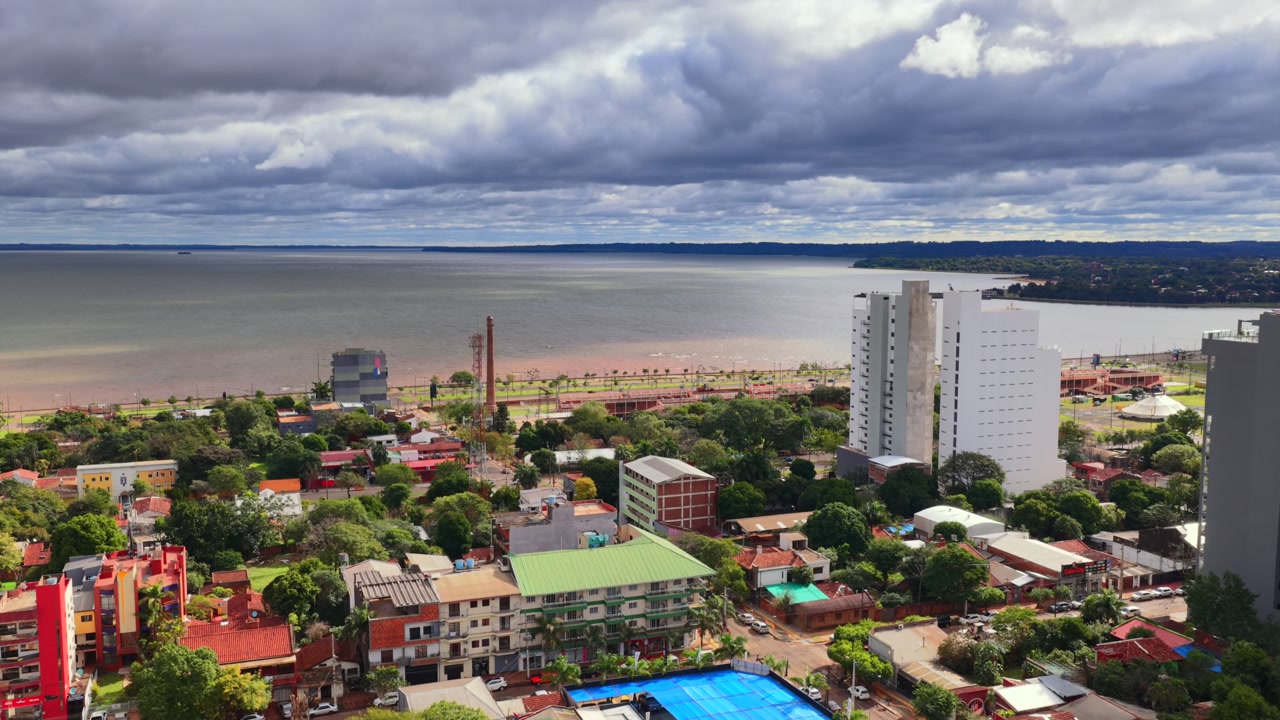 Encarnación cityscape with residential buildings and waterfront leading to the Paraná River near the Costanera. Aerial dolly in toward the river and skyline