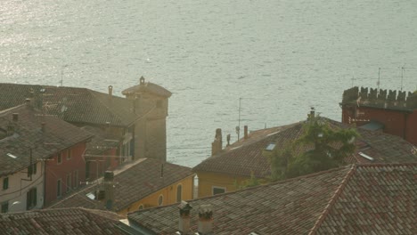 full shot, scenic view of the rooftop and chimneys of malcesine in italy, sun rises reflecting lago di garda in the back