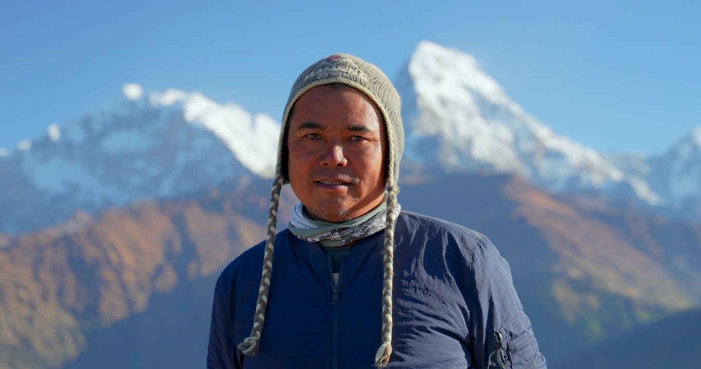 Annapurnan alue, Nepal, Muotokuva paikallisesta etniseen Gurung-heimoon kuuluvasta Himalajan kantajaoppaasta yllään villapipo, taustalla lumihuippuinen Annapurna South.