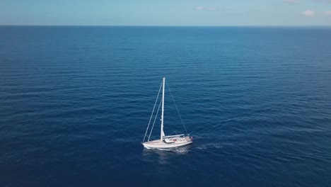 aerial top down shot of cruising oyster sailing boat on blue ocean in sunlight - orbiting shot