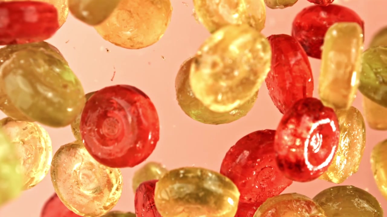 Caramelle colorate che galleggiano al rallentatore su uno sfondo rosa
