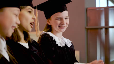 three happy little girls in cap and gown playing and laughing together at the preschool graduation ceremony