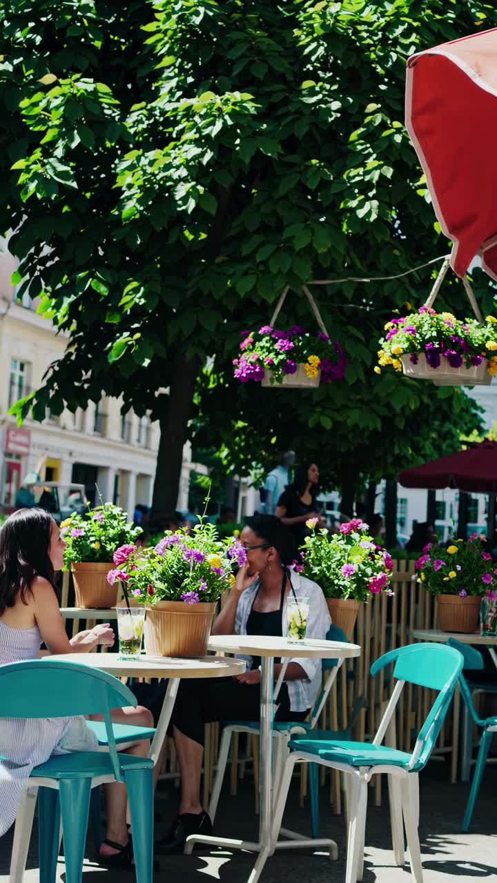 A lively outdoor cafe scene captured from a low angle, showcasing vibrant flowers and patrons