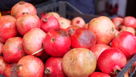 a man's hand picking a pomegranate from a basket of red pomegranates at a market