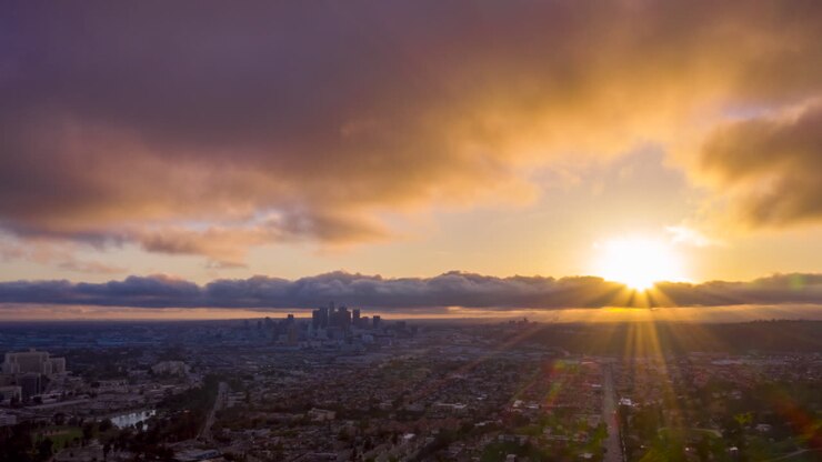 Hyperlapse de drone durante o pôr do sol sobre um subúrbio de Los Angeles, com a silhueta do horizonte do centro da cidade ao longe.