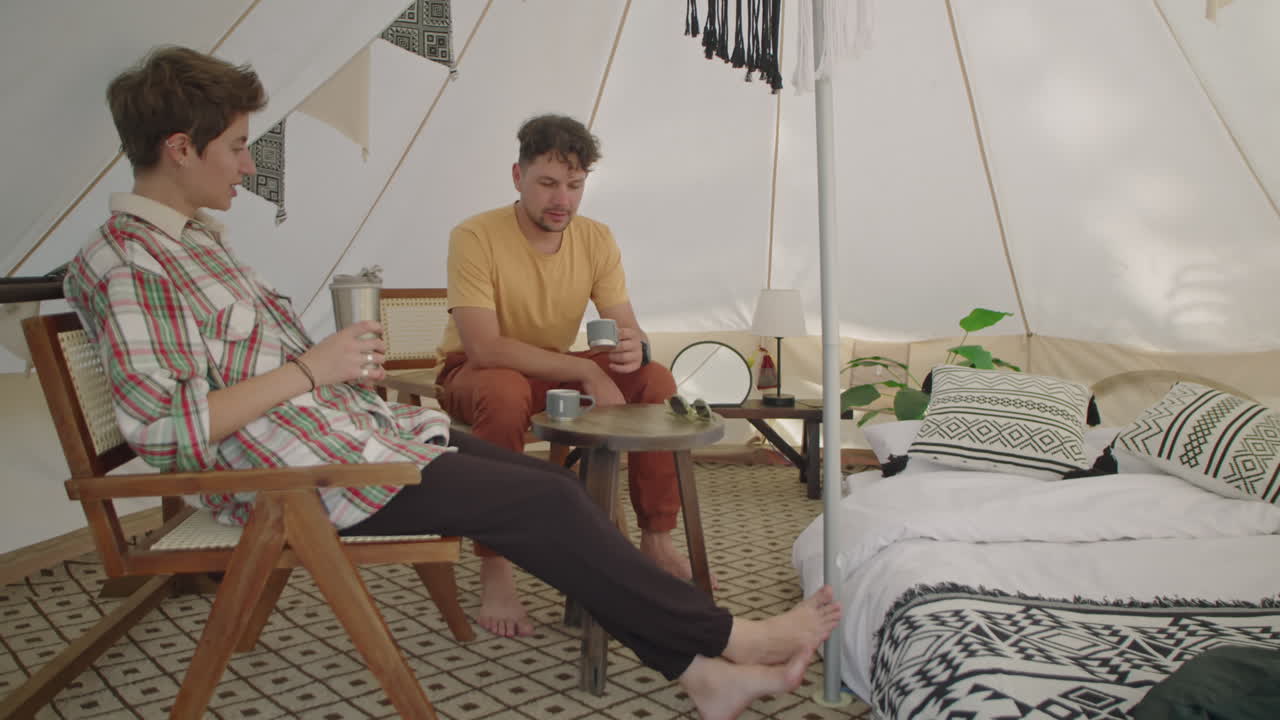 Uomo e donna che bevono tè e parlano in una tenda da glamping
