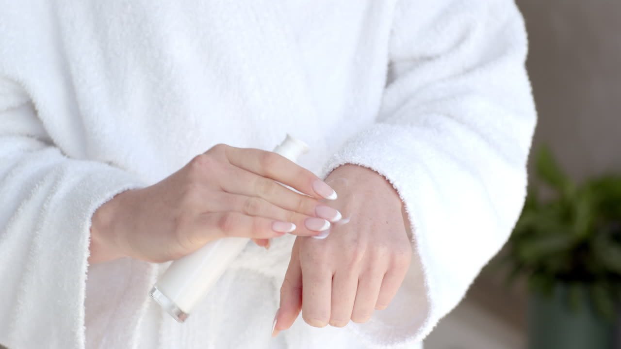 Applying lotion on hand, woman in bathrobe moisturizing skin at home