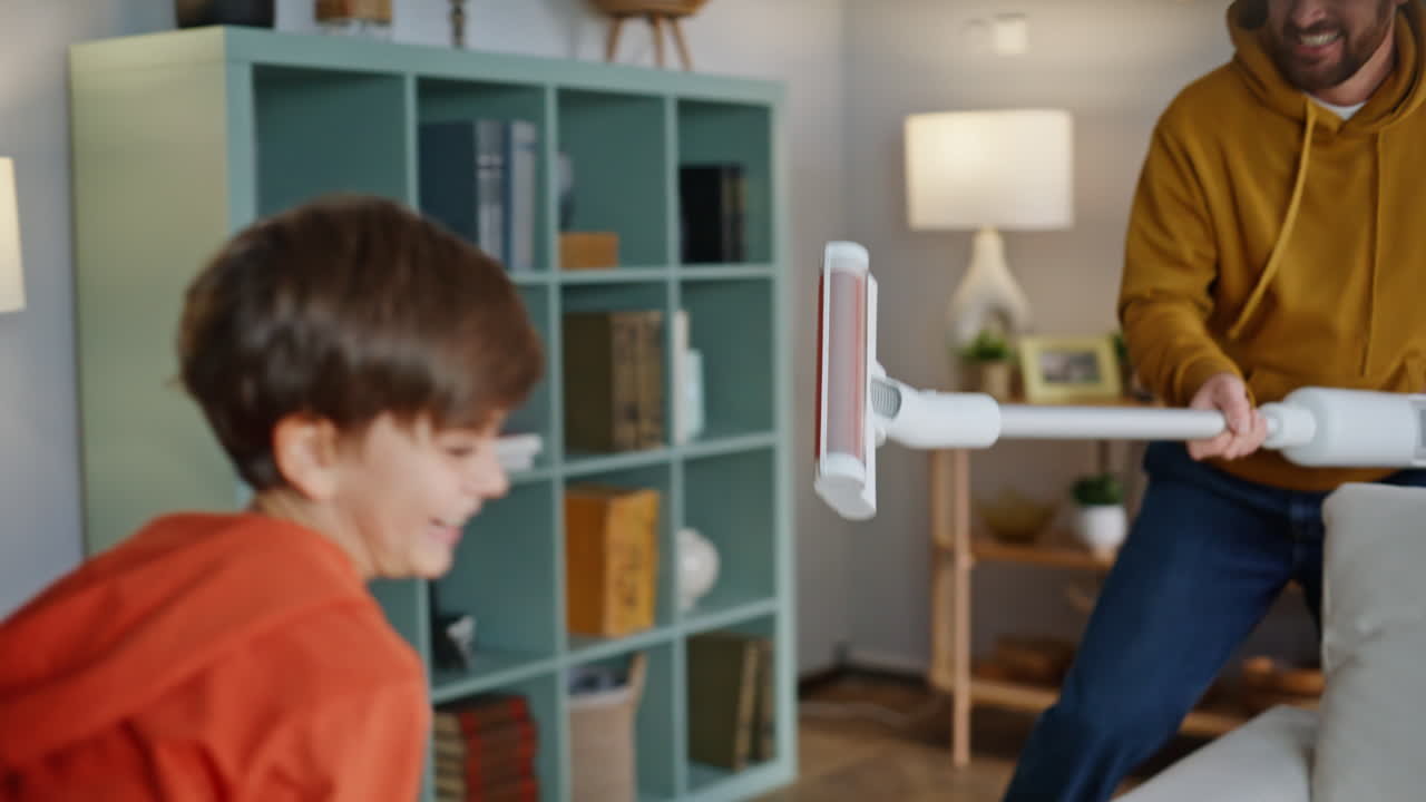 Cleaning father playing boy running after son holding vacuum cleaner closeup