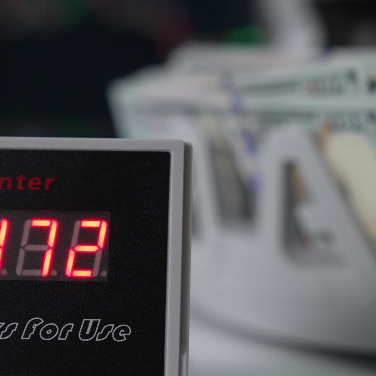 Red figures changing quickly on the screen of bill counter. Close up. Dollars being counted at backdrop in blur